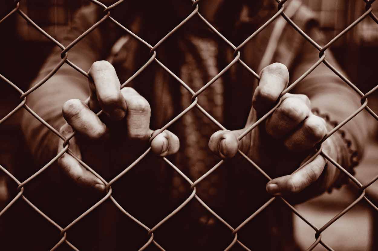 person putting fingers thru chainlink fence