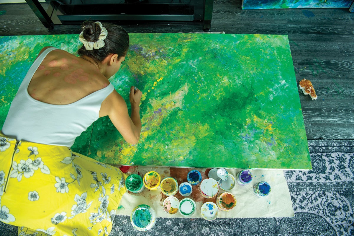 a woman in a yellow skirt paints a green abstract painting
