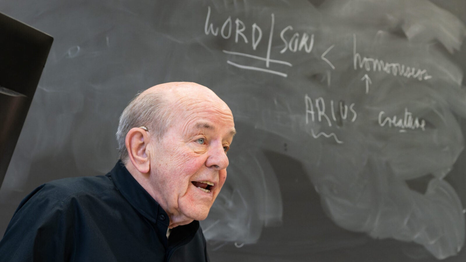 a priest stands in front of a chalkboard