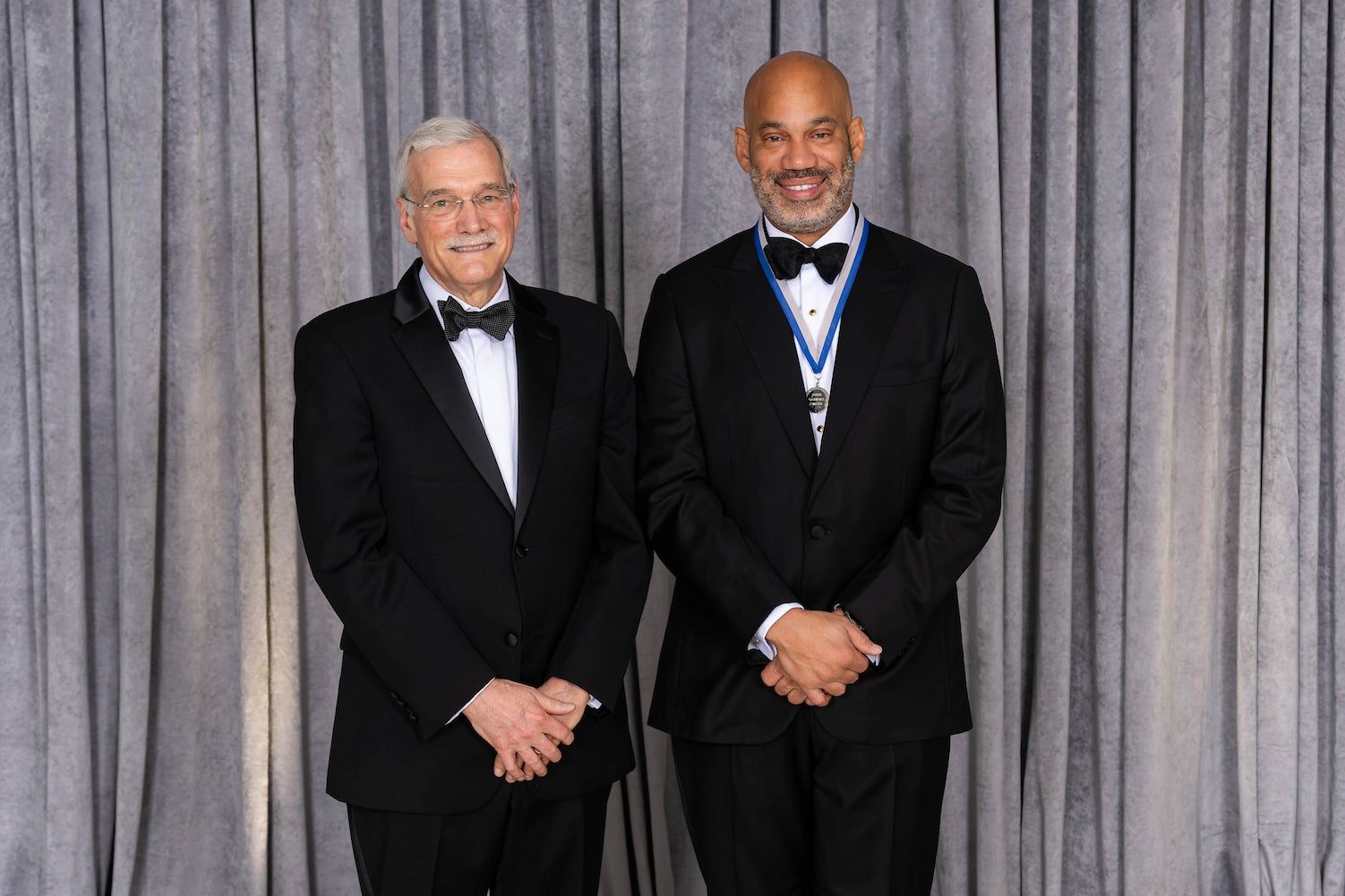 two men in tuxedos pose for a picture 