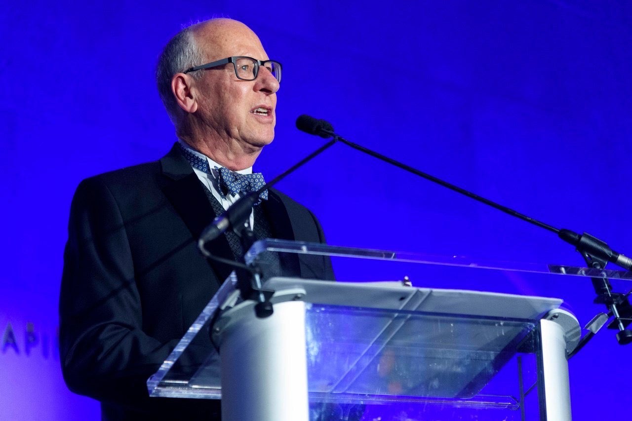 a man with glasses stands at a podium in front of a blue background