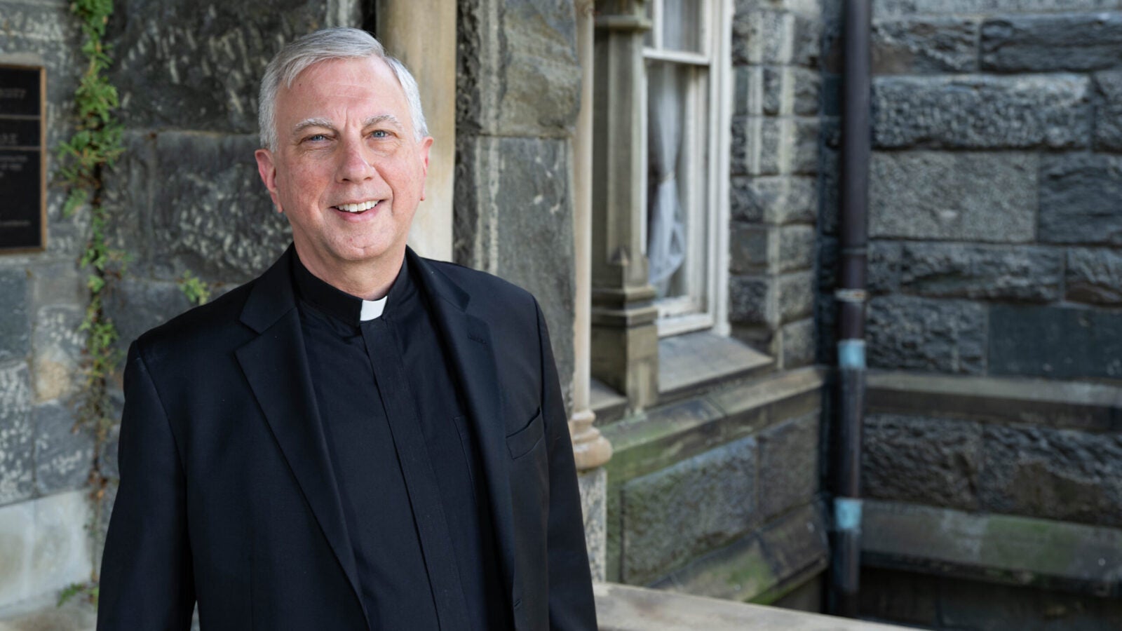 a man in clerical wear stands in front of a stone building